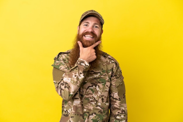 Military Redhead man over isolated on yellow background smiling