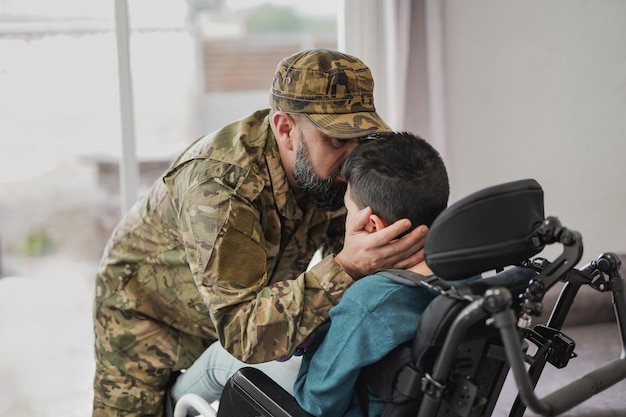 Военный солдат целует своего сына, сидящего в инвалидной коляске