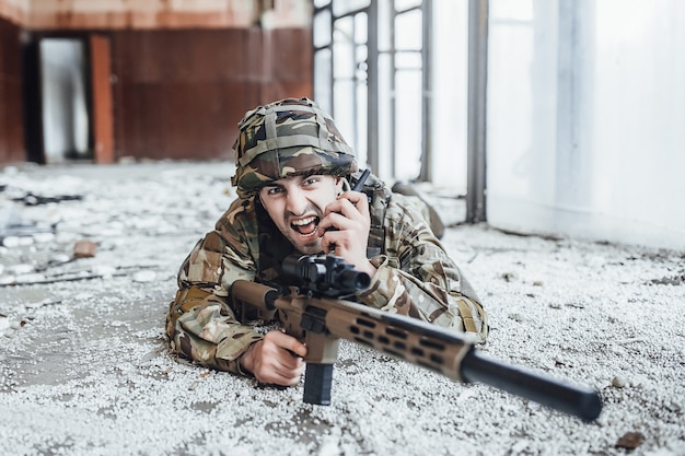 Солдат в военной форме лежит на земле и держит в руках большую винтовку