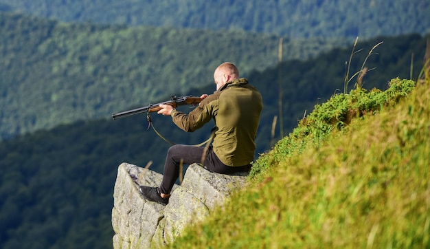 写真 ミリタリースタイルのカモフラージュの筋肉質の男性が武器の目的と成功を保持し、軍隊の狙撃兵が目標の山の兵士に到達し、フィールドポリゴンの男がハンターの趣味を発射する準備ができています