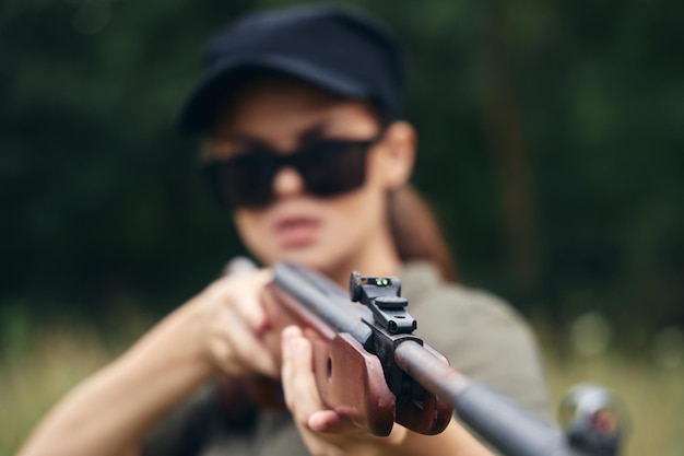 Military woman long gun sight aim hunting black cap green trees on background