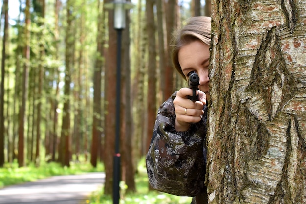 Военная женщина стреляет из ружья в лесу. девушка-охотник прячется за деревом с оружием.