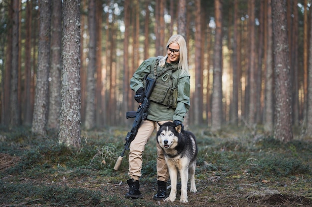 Foto donna militare con un fucile e un cane husky nella foresta