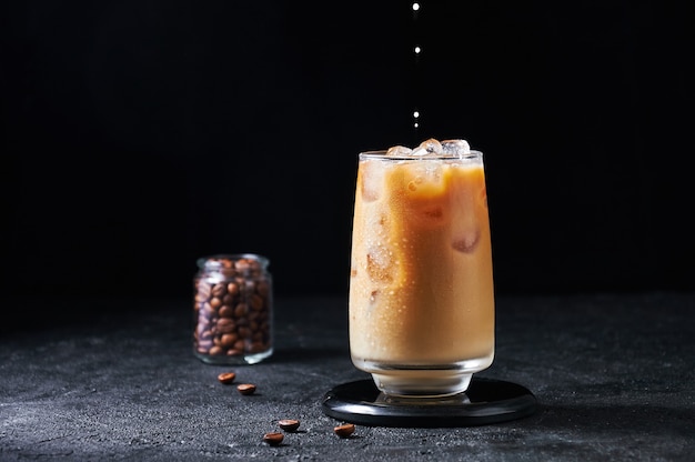 Milk Being Poured into Iced Coffee in Tall Glass on Dark Background. Concept Refreshing Summer Drink.