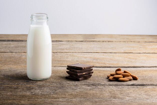 Milk in bottle, chocolate and almond on wooden