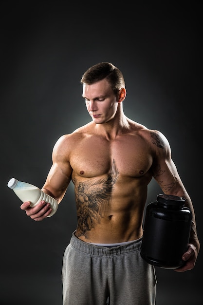 スポーツマン、適切な生活様式を持つ健康な人の手にある牛乳瓶。入れ墨