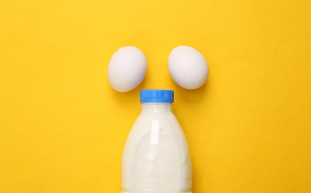 Milk bottle with eggs on yellow background