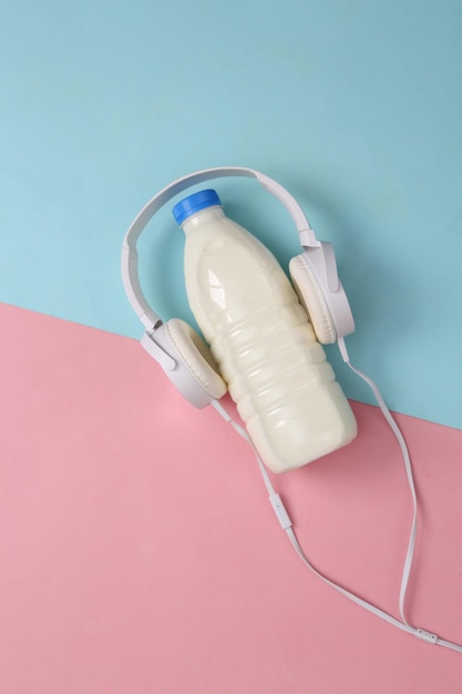 Milk bottle with headphones on bluepink pastel background Top view