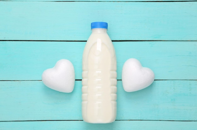 Milk bottle with hearts on blue wooden table Top view