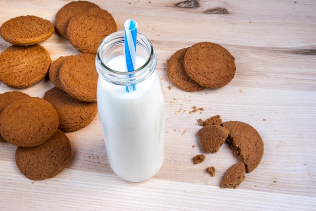 Milk bottle with straw and oatmeal cookies on wooden table