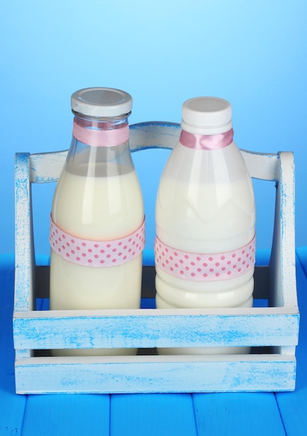 Photo milk in bottles in wooden box on blue wooden table on blue background