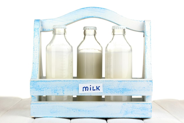 Milk in bottles in wooden box on wooden table on white background