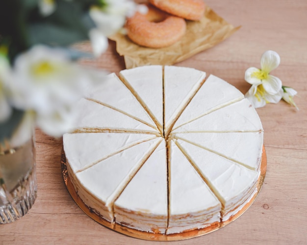 milk cake on a wooden table with flowers around top view