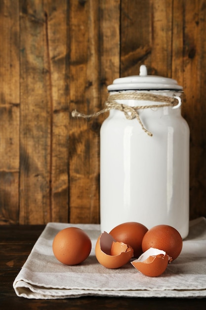 Молочная банка с яйцами и яичной скорлупой на деревенском деревянном фоне