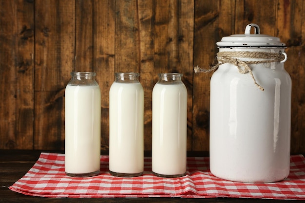 Milk can with glass bottles on napkin on rustic wooden background