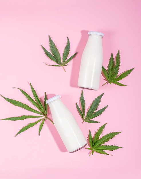 Milk cannabis supplement in a small bottle of hemp leaf on a pink background Vertical frame copy space Top view