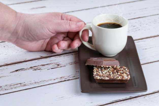 Barrette di cioccolato al latte con granella. sullo sfondo una donna che prende una tazza di caffè.