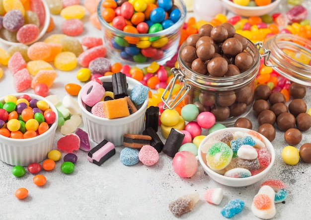 Milk chocolate candies woth shell in jar with various jelly gums candies on white table with liquorice allsorts and strawberry bonbons with different sour sugar gums