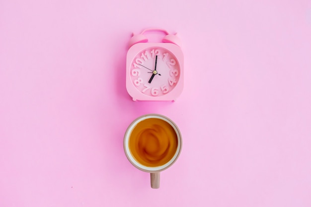 Foto caffè al latte e sveglia isolati su sfondo rosa, idea concettuale minima.