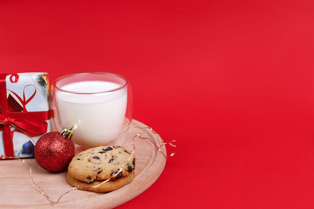 Milk, cookies with chocolate, and a New Year's gift on a red background