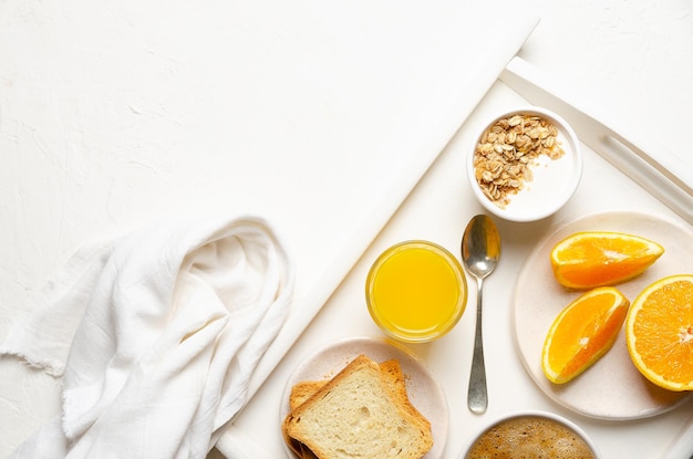 Milk a cup of coffee yoghurt orange juice and pieces of orange in a white tray and grey background