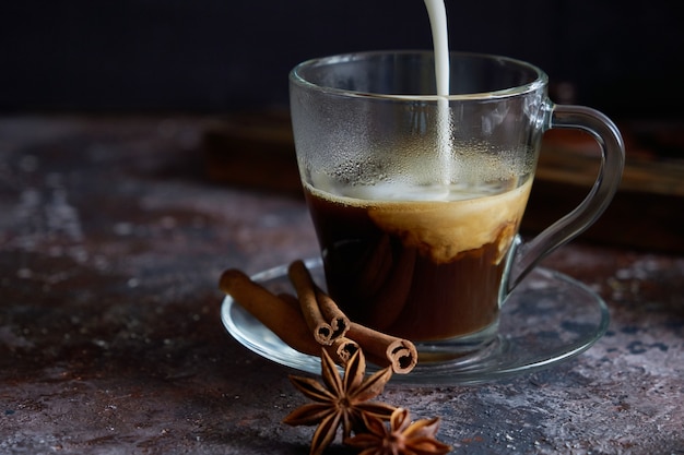 Milk foam is pouring into hot black coffee Cappuccino with sugar, cinnamon and anise