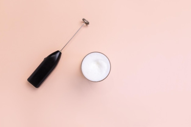 Foto creatore di schiuma di latte con bicchiere di latte su sfondo rosa pesca
