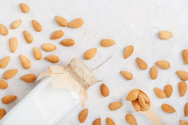 Milk from organic almonds in a transparent bottle with a scattering of seeds and a wooden spoon on a light background. Top view