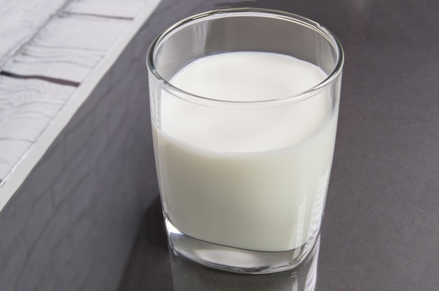 Milk in a glass cup on a black table, the reflection of the glass on the table.