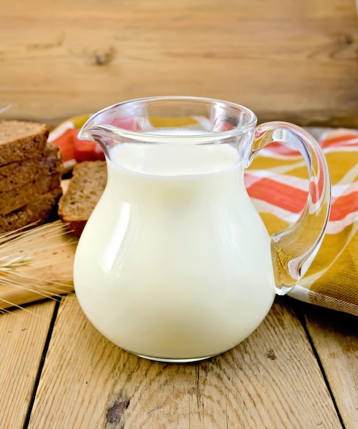 ライ麦パン、赤茶色の市松模様のナプキン、木の板の背景にライ麦スパイクとガラスの瓶にミルク