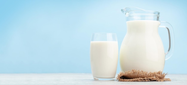 milk in glass and jug in front of wide blue background with copy space