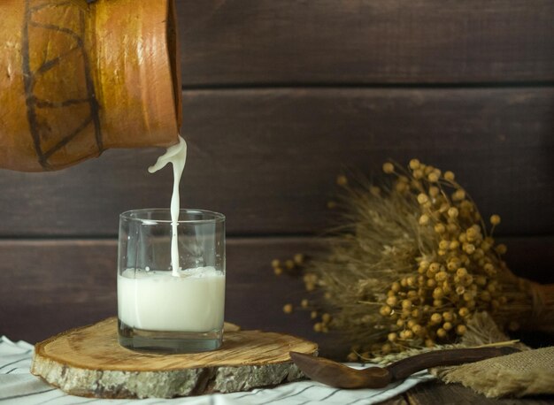 milk is poured from an earthenware jug into a glass on a rustic background