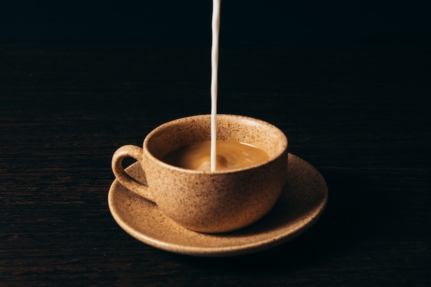 Milk is pouring into a cup of coffee on a black