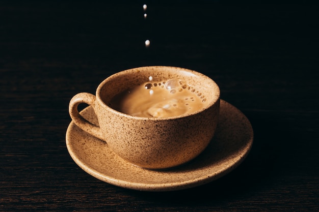 Milk is pouring into a cup of coffee on a black