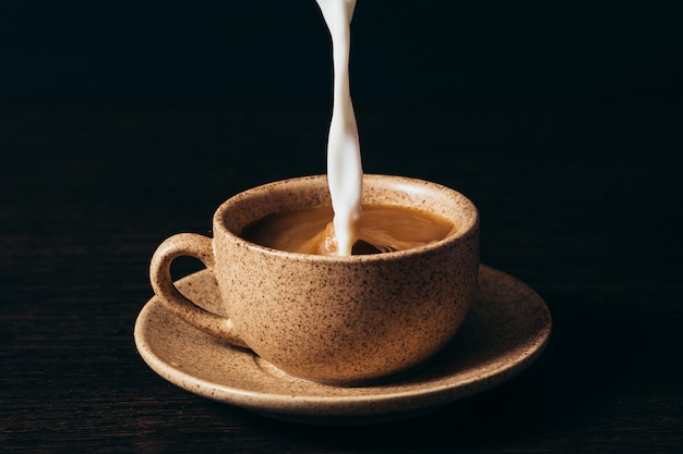 Milk is pouring into a cup of coffee on a black