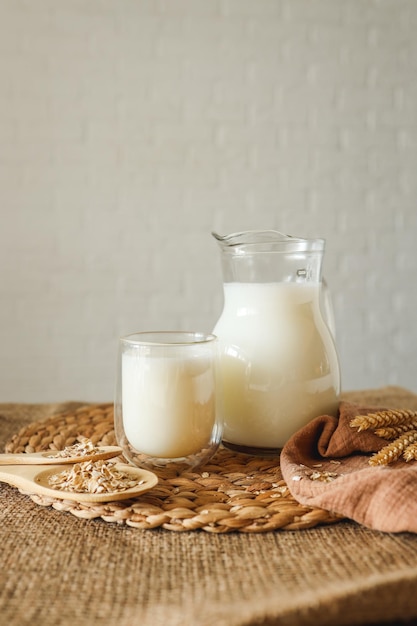 Молоко в кувшине и стакан деревянной ложкой с овсянкой и колосьями пшеницы на столе