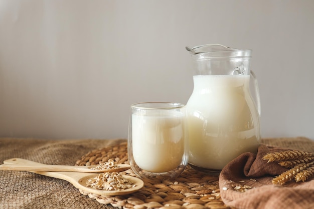 Milk in a jug and a glass a wooden spoon with oatmeal and ears of wheat on the table