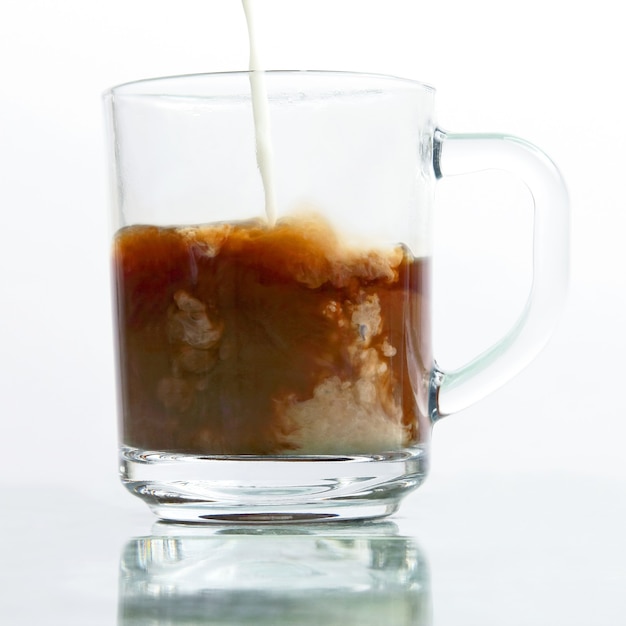 Milk poured into a transparent cup of black coffee. favorite hot drink