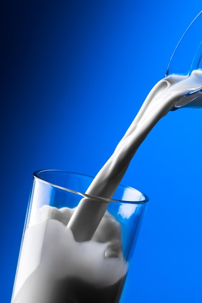 Молоко льется в стакан на синем фоне