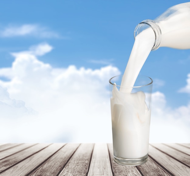 Milk pouring in glass on blurred tree background