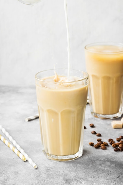 Milk pouring in ice coffee in a tall glass on a gray background