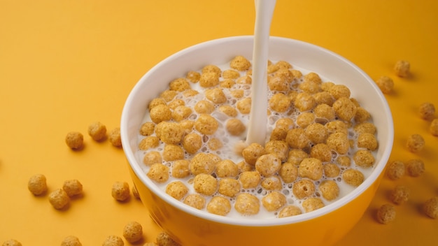 Milk pouring into bowl of corn ball flakes