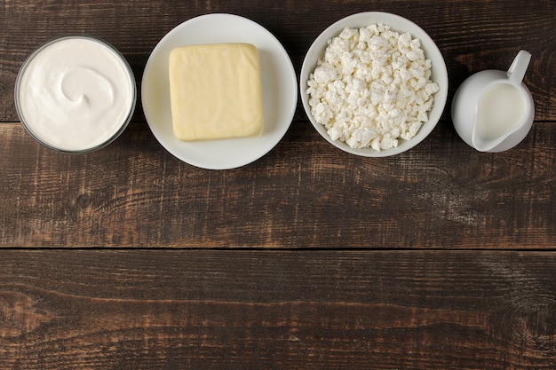 milk products. milk, sour cream, cheese, butter and cottage cheese on a brown wooden table. top view. frame. space for text