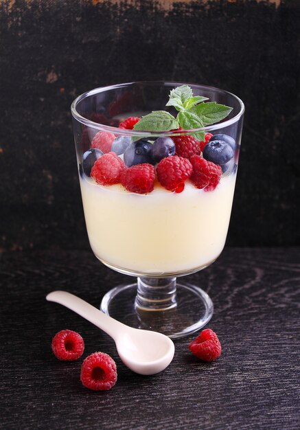 Milk pudding with berries in a glass on a black background