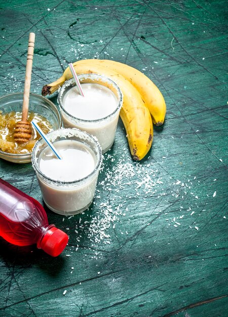 Milk smoothie with banana, strawberry syrup and honey. On rustic background.