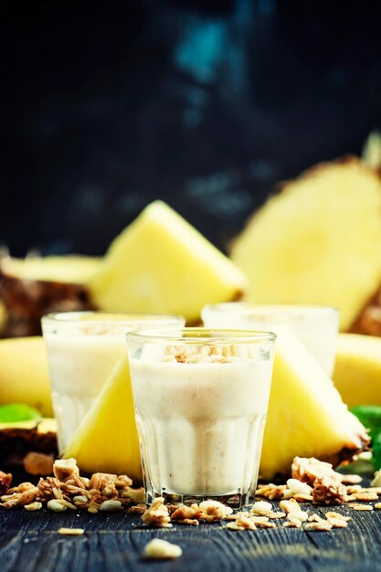 Milk smoothies with banana pineapple and granola dark background selective focus
