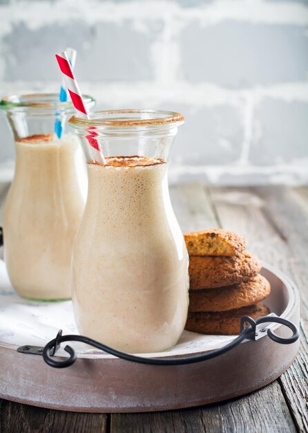 Milk vanilla smoothies with oatmeal cookies in glass jars on the old wooden background. Selective focus.