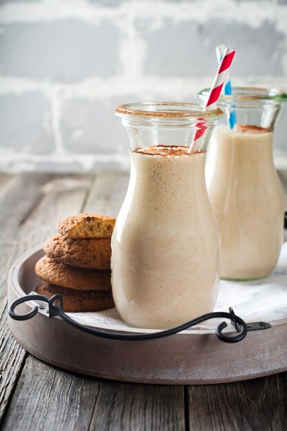 Milk vanilla smoothies with oatmeal cookies in glass jars on the old wooden surface. Selective focus.