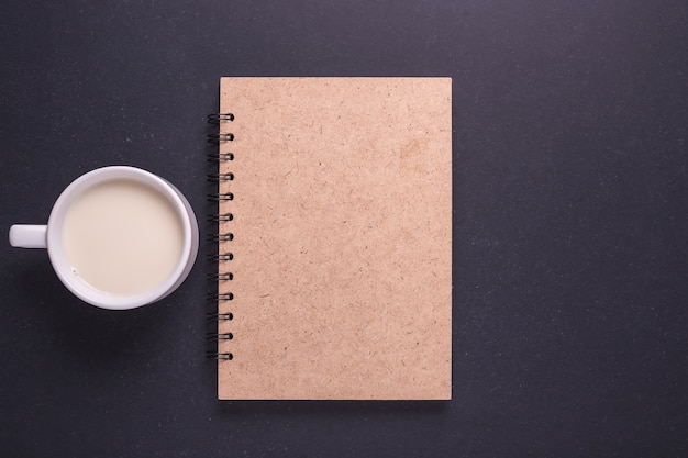 Milk in white glass and brown note book on black stone table background