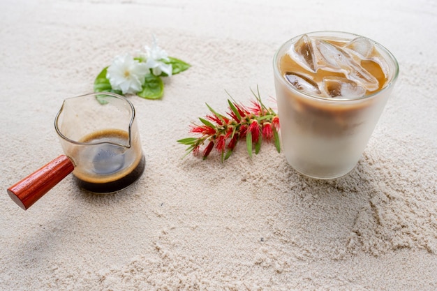 Milk with coffee on sand beach next to bottle brush\
flower.